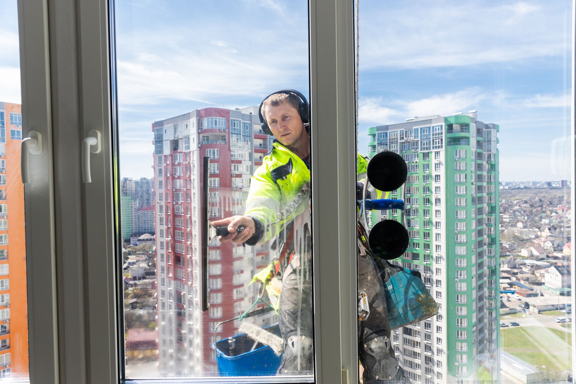 A Professional Window Cleaner at Work on a High-Rise Building, Demonstrating Safety and Skill While Cleaning Glass Windows with a Stunning Cityscape Background
